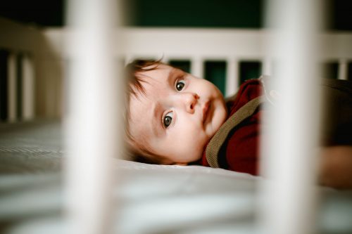 baby in red and gray hoodie lying on white bed