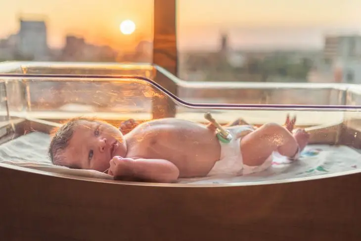 baby in white disposable diaper lying on white bathtub