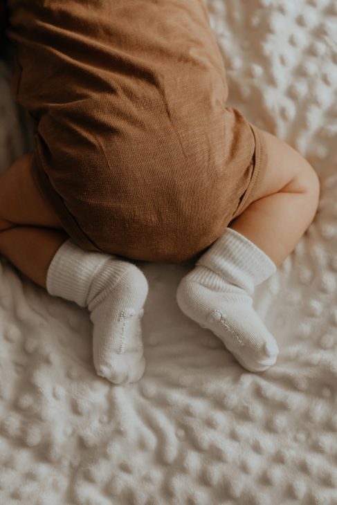 baby in white socks lying on bed