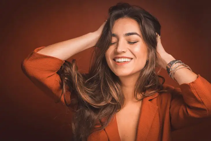 smiling woman in brown top holding hair