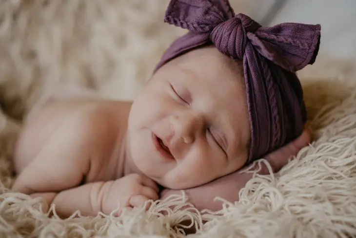 baby in purple knit cap lying on white fur textile