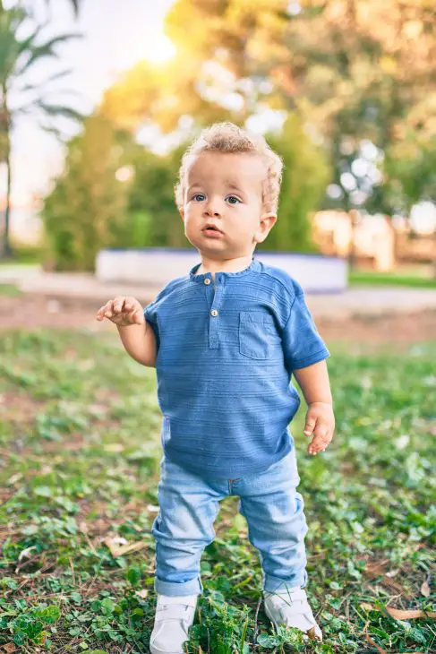Cute and happy little boy having fun at the park on a sunny day. Beautiful blonde hair male toddler playing outdoors